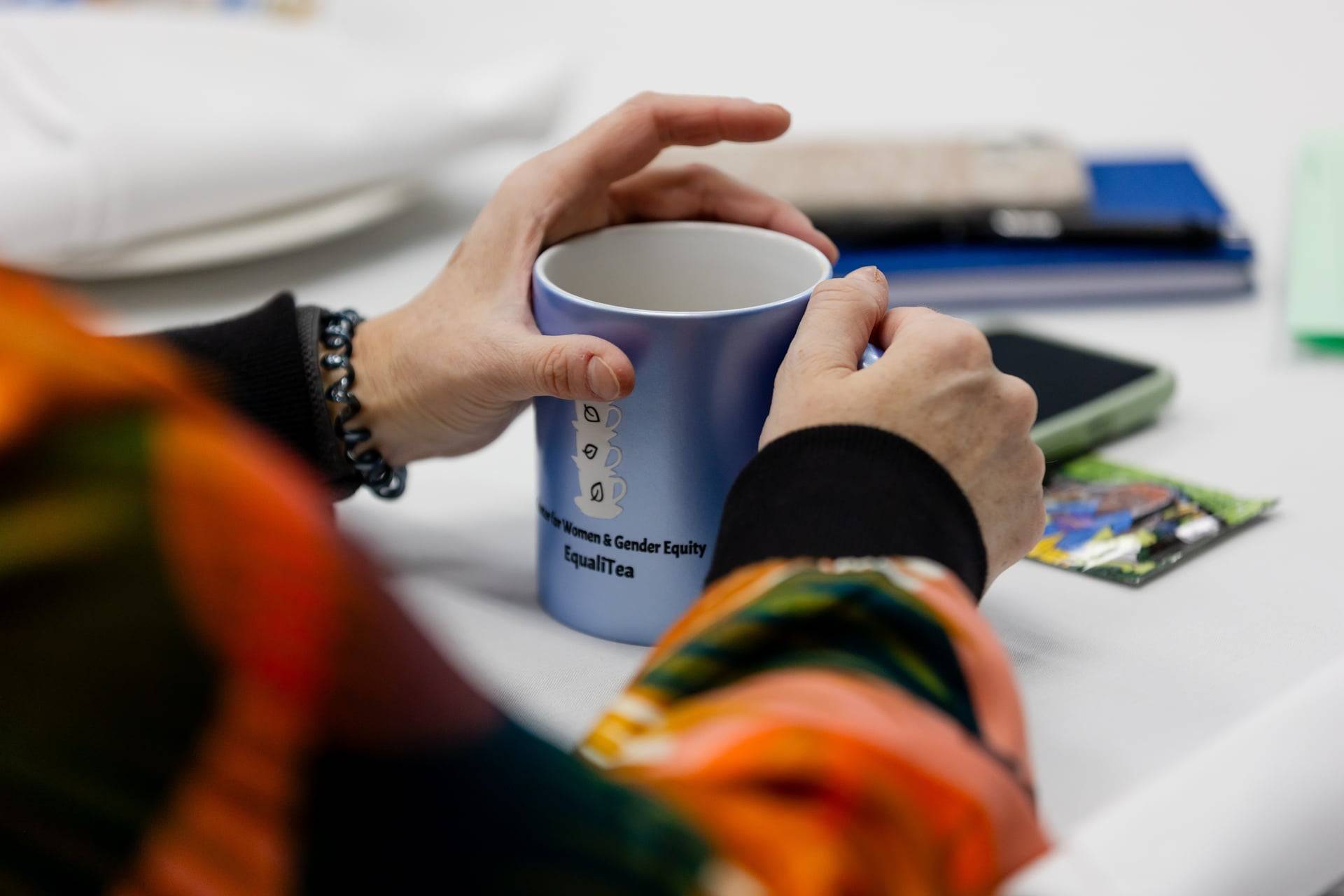Photo shows two hands wrapped around a blue mug with lettering that reads "EqualiTEA" Center for Women & Gender Equity